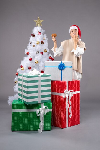 Jeune femme tenant des biscuits sur un sol gris près de l'arbre de Noël et des cadeaux