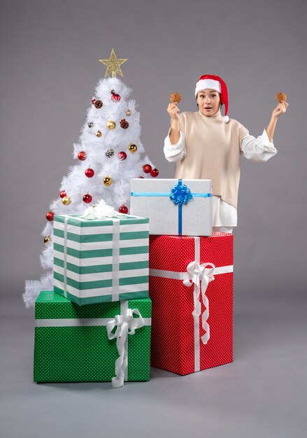 Jeune femme tenant des biscuits sur un sol gris près de l'arbre de Noël et des cadeaux