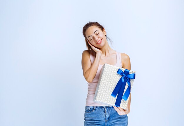 Jeune femme tenant une boîte-cadeau blanche enveloppée d'un ruban bleu et a l'air fatiguée et épuisée