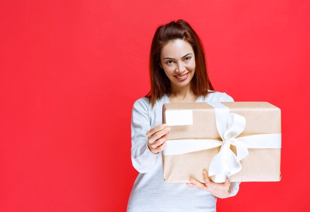 Jeune femme tenant une boîte-cadeau en carton et présentant sa carte de visite