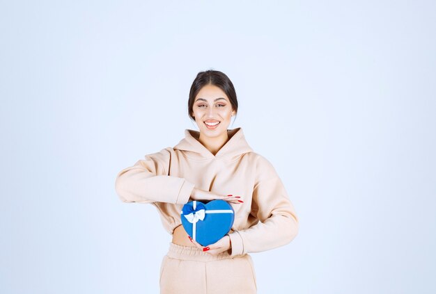 Jeune femme tenant une boîte-cadeau en forme de coeur bleu et a l'air heureux