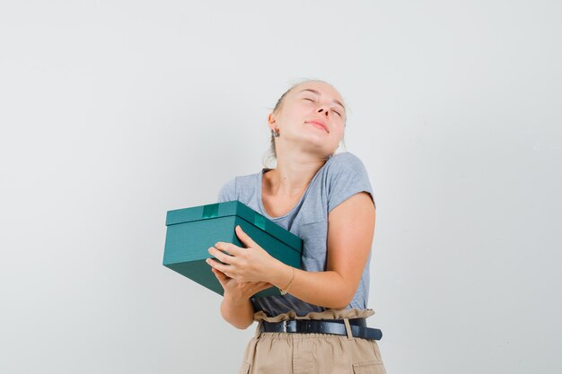 Jeune femme tenant une boîte cadeau en t-shirt et pantalon et à la joyeuse