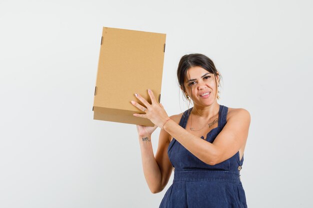 Jeune femme tenant une boîte en carton en robe et semblant heureuse