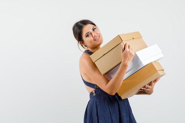 Jeune femme tenant des boîtes en carton en robe et semblant joyeuse