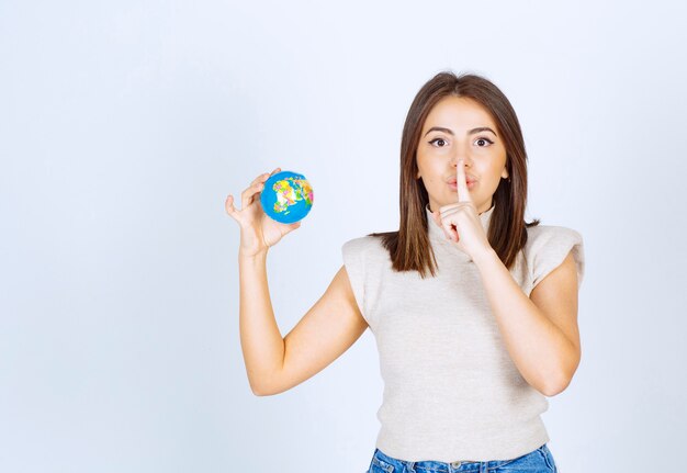 Jeune femme tenant une boule de globe terrestre et faisant un signe silencieux.