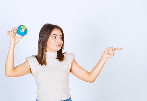 Jeune femme tenant une boule de globe terrestre et pointant vers l'extérieur avec un index