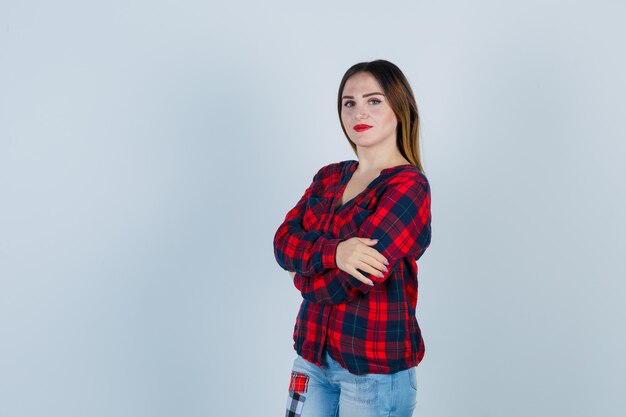 Jeune femme tenant les bras croisés en chemise à carreaux et l'air confiant. vue de face.