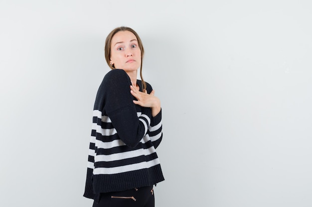 Jeune femme tenant les bras croisés sur la poitrine en maille rayée et pantalon noir et à la surprise