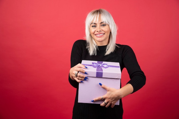 Jeune femme tenant un cadeau sur un mur rouge.