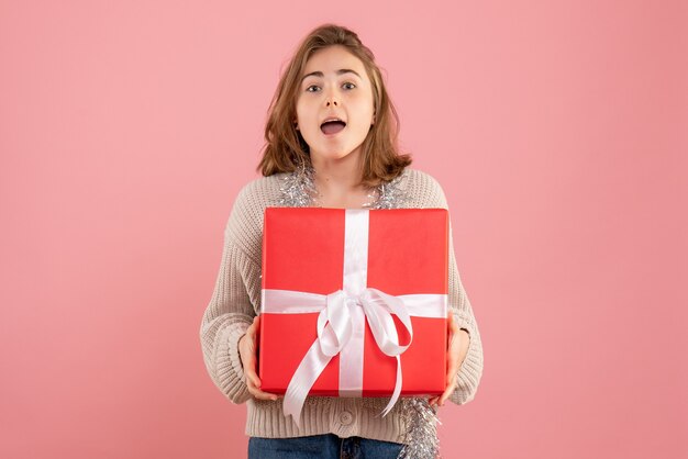 jeune femme tenant un cadeau de Noël dans ses mains sur rose