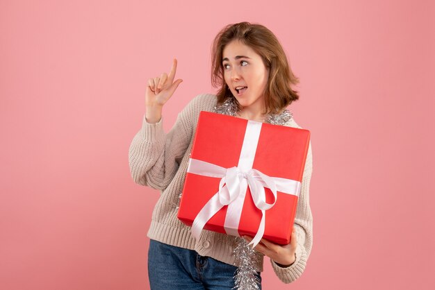 jeune femme tenant un cadeau de Noël dans ses mains sur rose