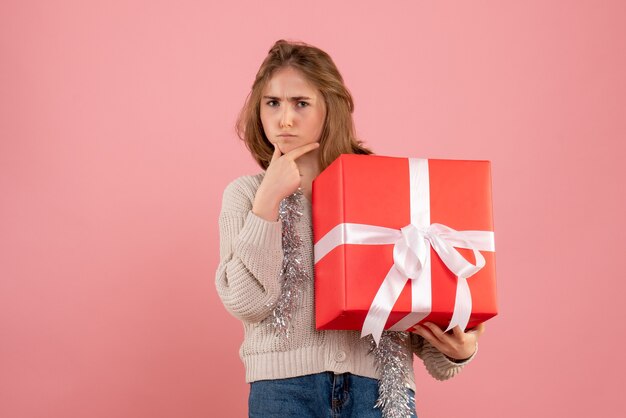jeune femme tenant un cadeau de Noël dans ses mains sur rose