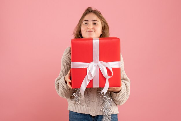 jeune femme tenant un cadeau de Noël dans ses mains sur rose