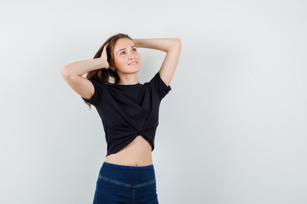 Jeune femme tenant les cheveux avec les mains en chemisier noir, pantalon et à la joyeuse.