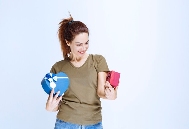 Jeune femme tenant des coffrets cadeaux bleus en forme de coeur et rouge et les appréciant