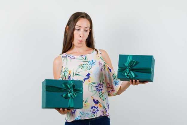 Jeune femme tenant des coffrets cadeaux en chemise, jeans et regardant étonné, vue de face.