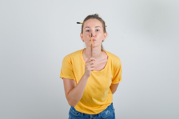 Jeune femme tenant un crayon de dessin en t-shirt jaune, short en jean et à heureux