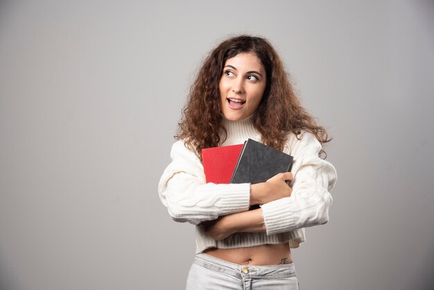 Jeune femme tenant deux livres sur un mur gris. Photo de haute qualité