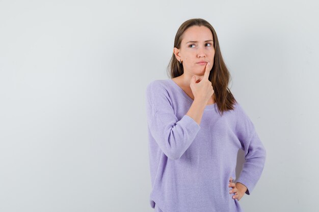 Jeune femme tenant le doigt sur le menton en chemise décontractée et à la pensif. vue de face.