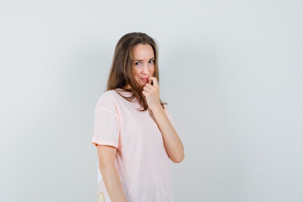 Jeune femme tenant le doigt sur sa lèvre en t-shirt rose et à la honte. vue de face.