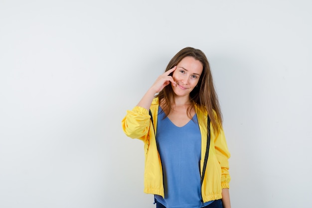 Jeune femme tenant le doigt sur les tempes en t-shirt, veste et semblant intelligente, vue de face.