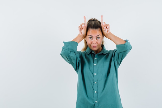 Jeune femme tenant les doigts sur la tête comme des cornes de taureau en chemisier vert et à mignon