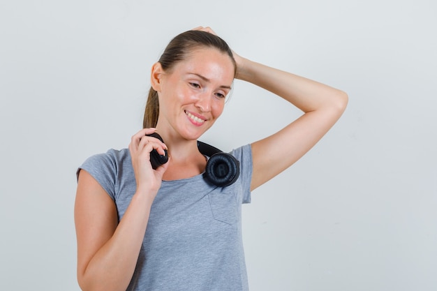 Jeune femme tenant des écouteurs en t-shirt gris et à la vue de face, heureux.