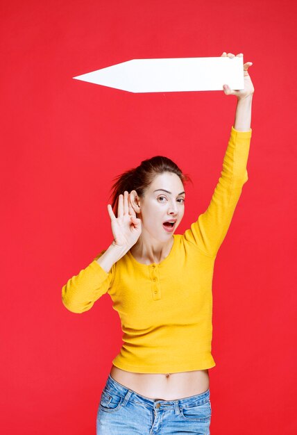 Jeune femme tenant une flèche pointant vers la gauche et écoutant attentivement