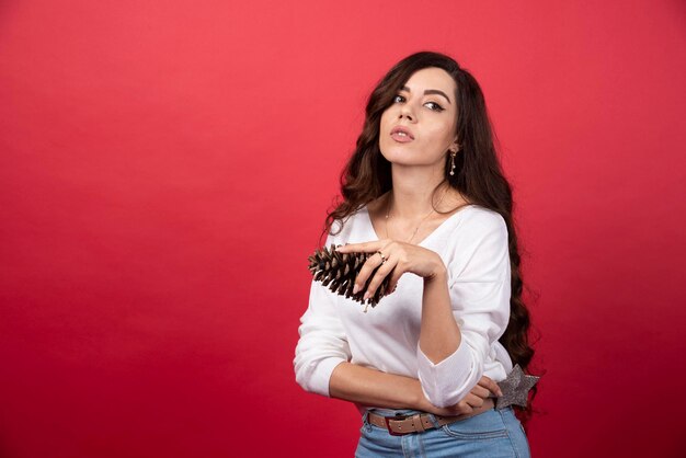 Jeune femme tenant une grosse pomme de pin de Noël sur fond rouge. photo de haute qualité