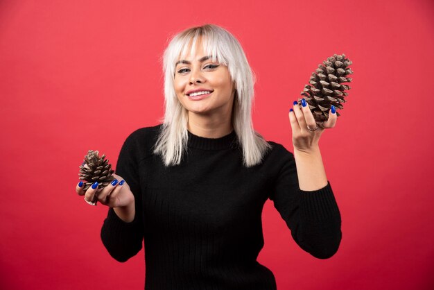 Jeune femme tenant de grosses pommes de pin sur un mur rouge.