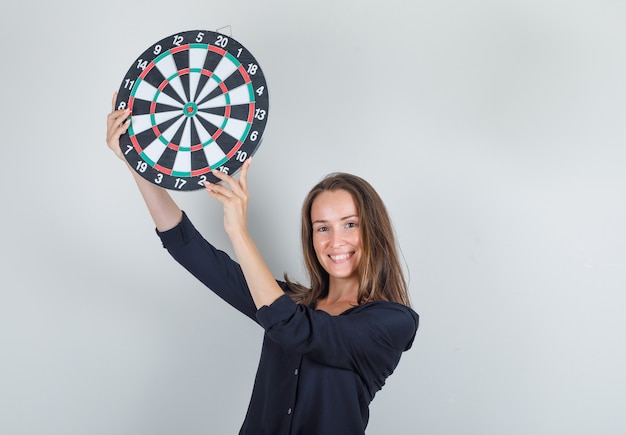 Photo gratuite jeune femme tenant un jeu de fléchettes en chemise noire et à la joyeuse