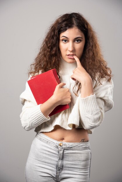 Photo gratuite jeune femme tenant un livre rouge sur un mur gris. photo de haute qualité