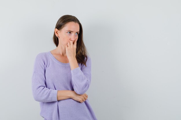 Jeune femme tenant la main sur la bouche en chemise décontractée et à la pensif. vue de face.