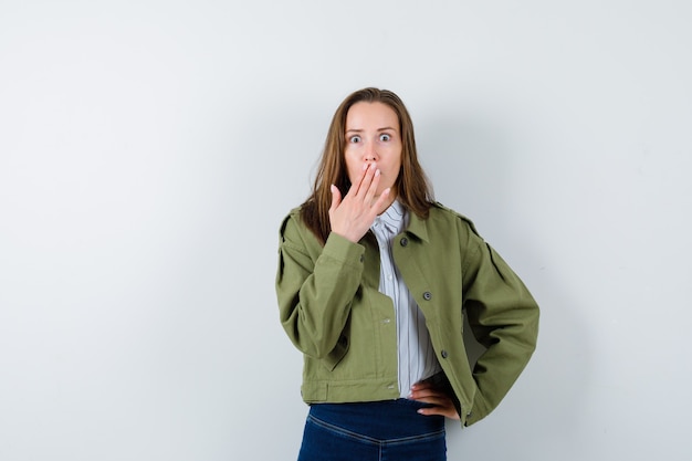 Jeune femme tenant la main sur la bouche en chemise, veste et à la surprise. vue de face.