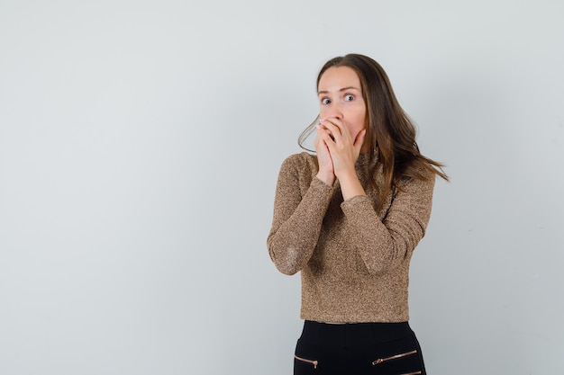 Jeune femme tenant la main sur la bouche en chemisier doré et à la vue de face, excité. espace pour le texte