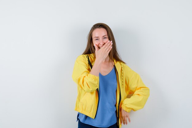 Jeune femme tenant la main sur la bouche en t-shirt et l'air heureux, vue de face.