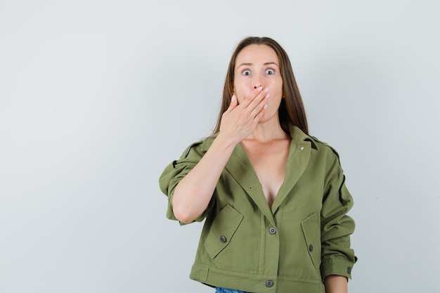 Jeune femme tenant la main sur la bouche en veste verte et à la surprise. vue de face.