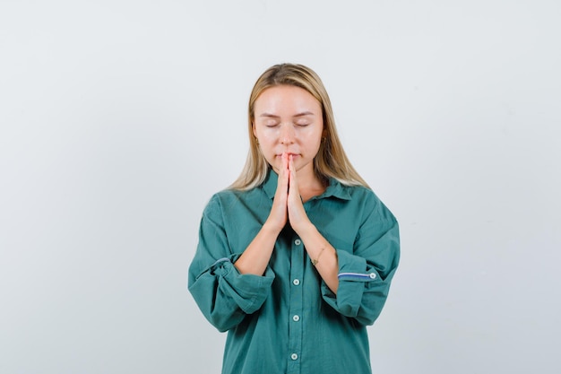 Jeune femme tenant la main dans un geste de prière en chemise verte et l'air paisible.