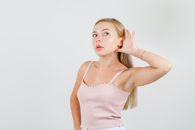 Jeune femme tenant la main derrière l'oreille en maillot, mini jupe et à la recherche de sérieux.