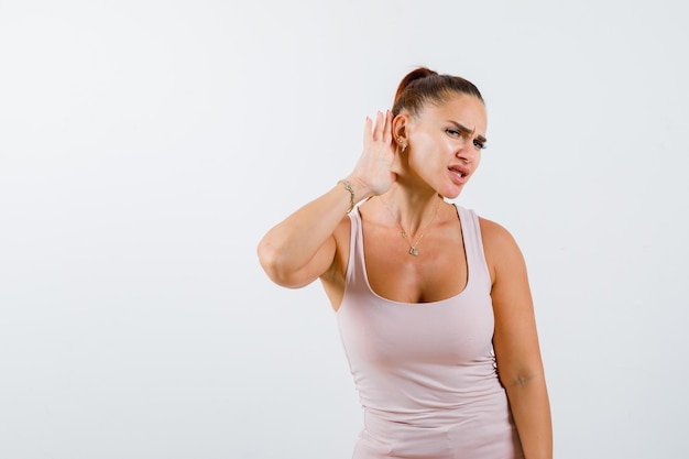 Jeune femme tenant la main derrière l'oreille en maillot et à la perplexité, vue de face.