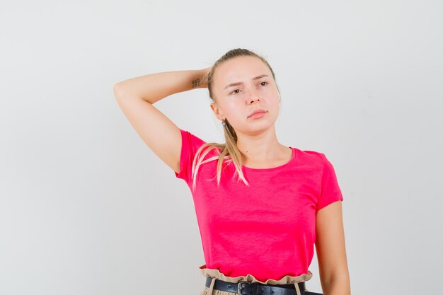 Jeune femme tenant la main derrière la tête en t-shirt et pantalon et à la pensive