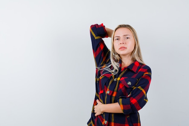 Jeune femme tenant la main derrière la tête tout en gardant la main sur le ventre en chemise à carreaux et à la vue de face confiante.