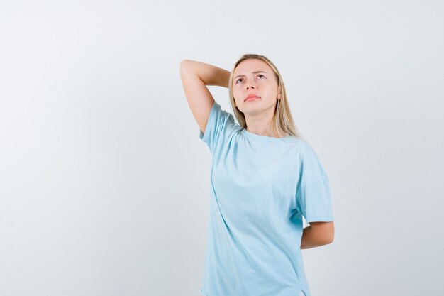 Jeune femme tenant la main derrière la tête tout en regardant en t-shirt et à la réflexion. vue de face.