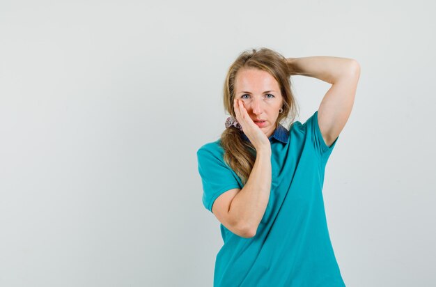 Jeune femme tenant la main derrière la tête tout en touchant le visage en t-shirt et à la réflexion.