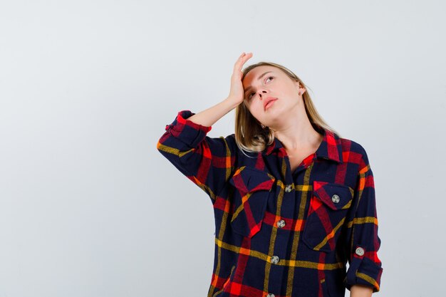 Jeune femme tenant la main sur le front tout en regardant en chemise à carreaux et à la recherche attentionnée. vue de face.