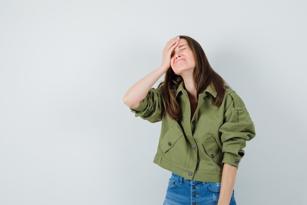 Jeune femme tenant la main sur le front en veste, short et à la vue de face, oublieux.