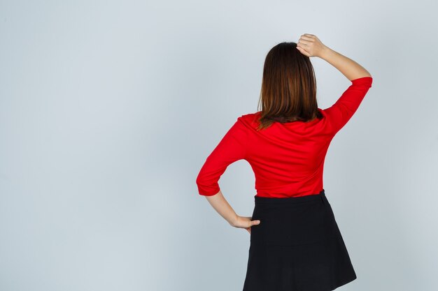 Jeune femme tenant la main sur la hanche, mettant la main sur la tête en chemisier rouge