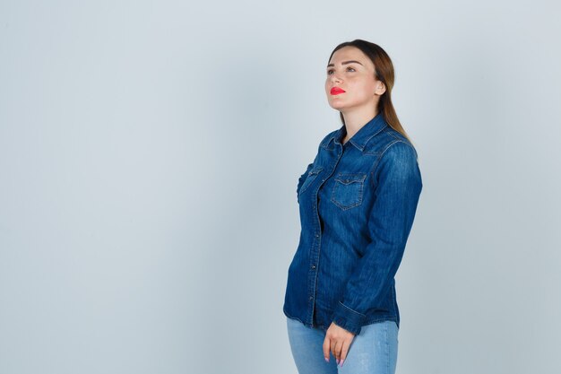 Jeune femme tenant la main sur la hanche tout en regardant ailleurs en chemise en jean et jeans et à la réflexion