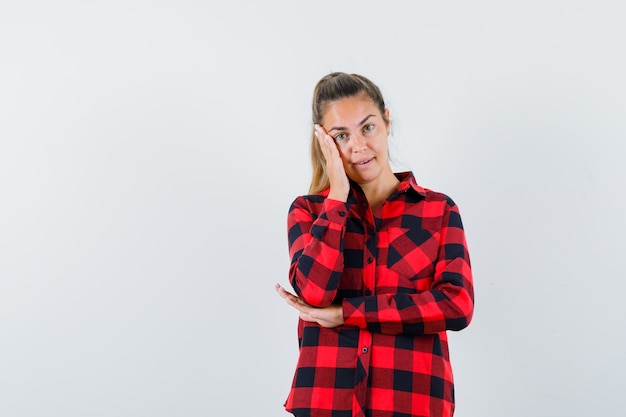 Jeune femme tenant la main sur la joue en chemise décontractée et à la jolie vue de face.