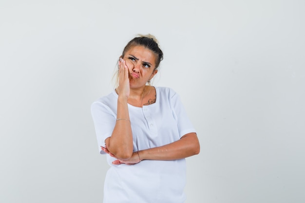 Jeune femme tenant la main sur la joue en t-shirt et à la pensif